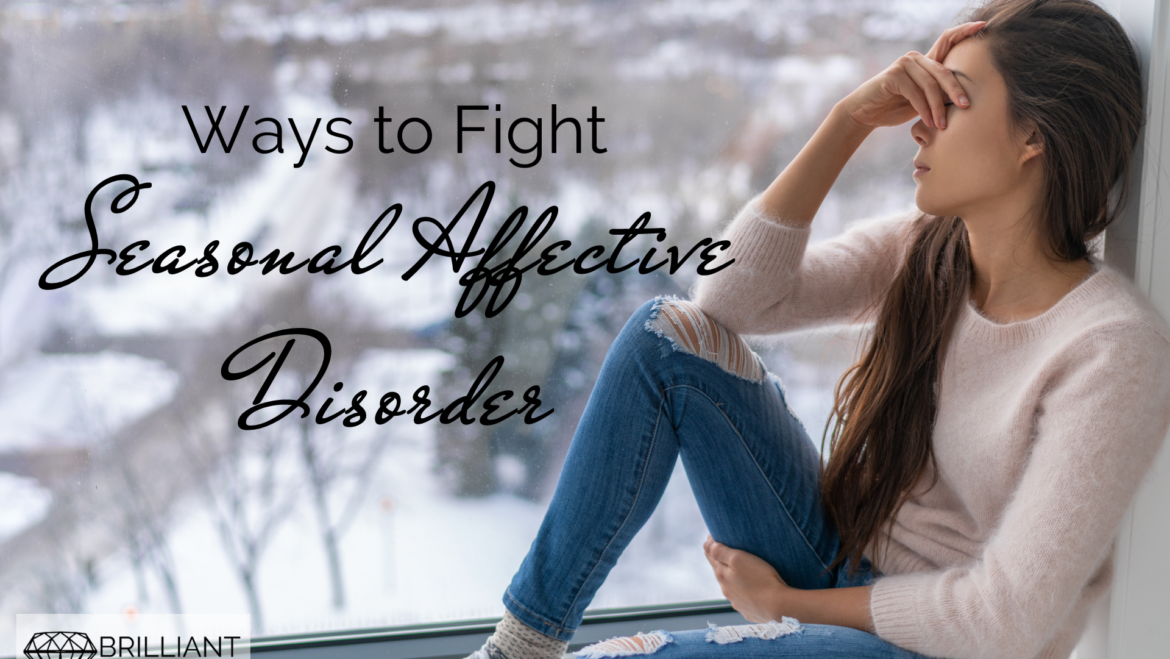 girl sitting by the window covering her face by her hand with snow outside: te seasonal affective disorderxt: ways to fight