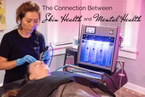 a licensed esthetician in black uniform giving a Hydrafacial to a client lying in a facial bed: text: the connection between skin health and mental health
